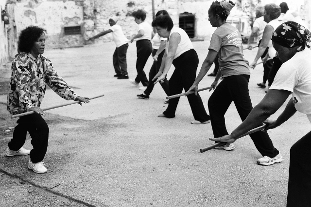 Black and white image of a group of people exercising with wooden poles. 